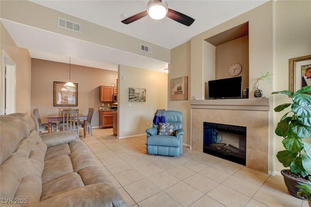 living room with ceiling fan, a tiled fireplace, and light tile patterned flooring