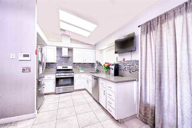 kitchen featuring vaulted ceiling, white cabinetry, wall chimney range hood, sink, and stainless steel appliances