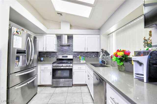 kitchen with vaulted ceiling with skylight, white cabinetry, wall chimney range hood, stainless steel appliances, and sink