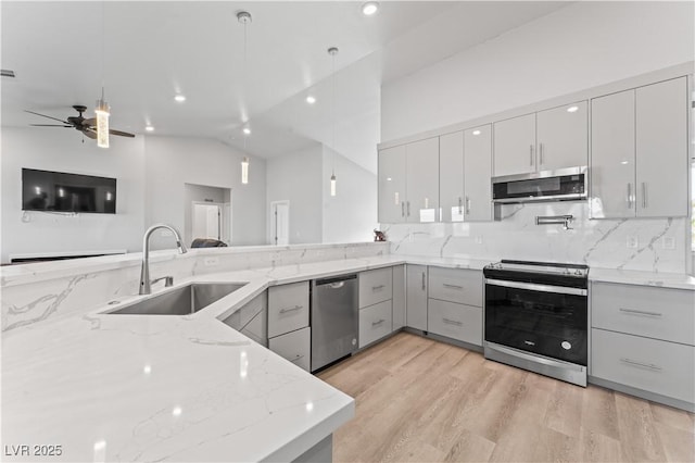 kitchen with sink, light wood-type flooring, kitchen peninsula, stainless steel appliances, and light stone countertops