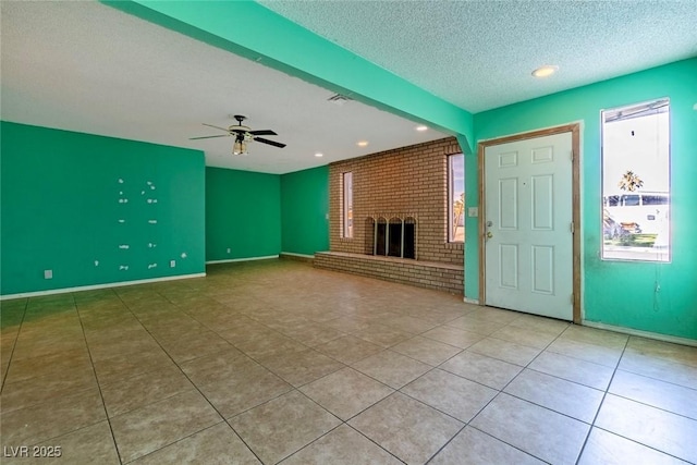 unfurnished living room with ceiling fan, light tile patterned floors, a fireplace, and a textured ceiling