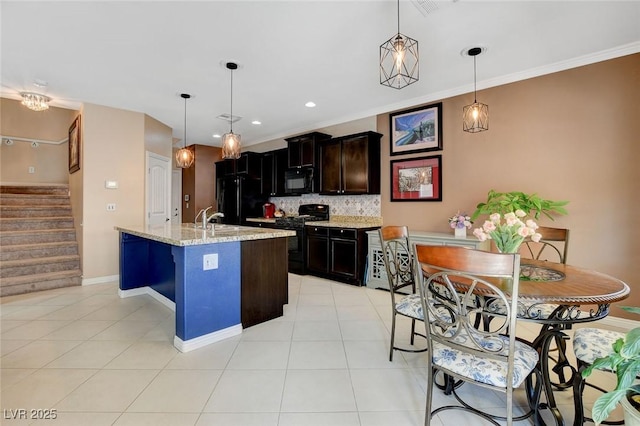 kitchen featuring light stone counters, hanging light fixtures, black appliances, and a center island with sink