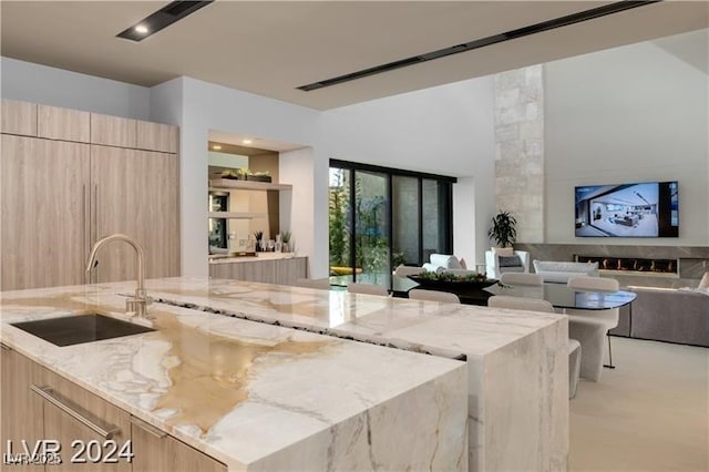 kitchen with light stone counters, sink, light brown cabinets, and a center island with sink