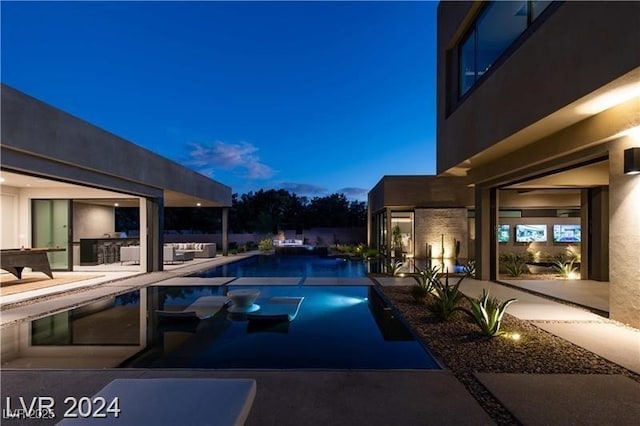 pool at dusk featuring a patio and exterior kitchen