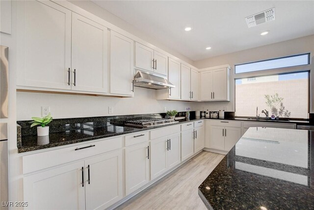 kitchen featuring white cabinets, stainless steel gas cooktop, dark stone counters, and light wood-type flooring