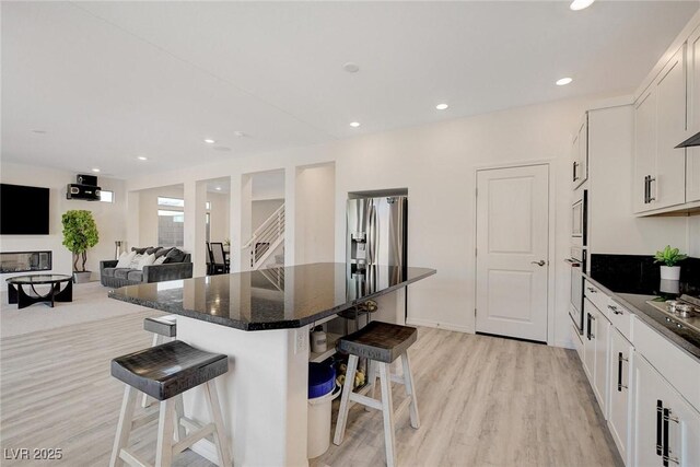 kitchen featuring stainless steel refrigerator with ice dispenser, white oven, white cabinets, a kitchen island, and a breakfast bar area