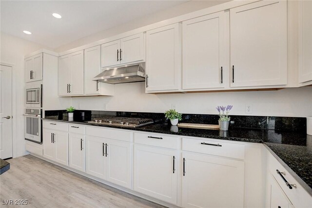 kitchen with white cabinetry, stainless steel appliances, dark stone countertops, and light hardwood / wood-style flooring