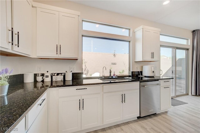 kitchen featuring dishwasher, a sink, dark stone counters, white cabinets, and light wood-type flooring