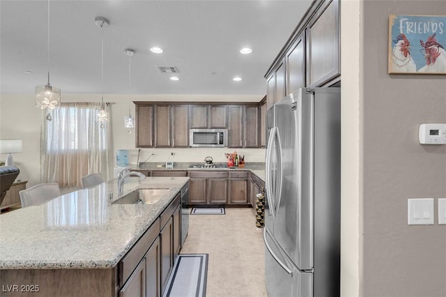 kitchen featuring appliances with stainless steel finishes, decorative light fixtures, sink, light stone countertops, and a center island with sink