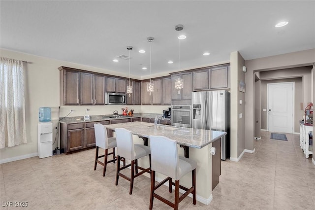 kitchen with a kitchen island with sink, dark brown cabinets, pendant lighting, a breakfast bar, and stainless steel appliances