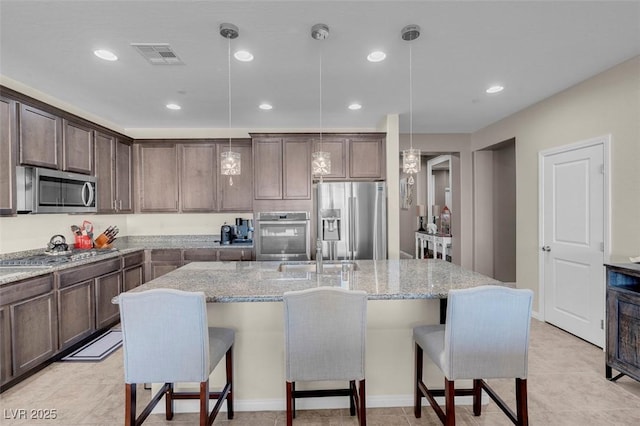 kitchen with dark brown cabinets, pendant lighting, stainless steel appliances, and a kitchen island with sink