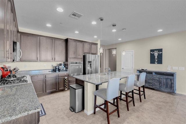 kitchen featuring hanging light fixtures, a kitchen island with sink, sink, stainless steel appliances, and light stone counters