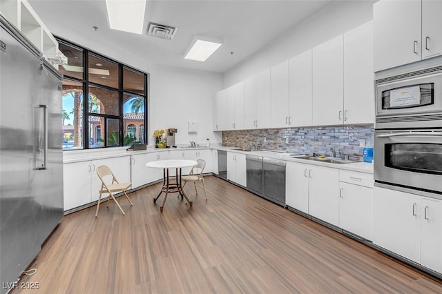 kitchen featuring wood-type flooring, white cabinetry, built in appliances, sink, and backsplash