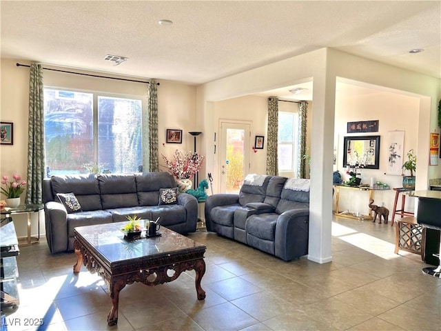 living room with a textured ceiling, light tile patterned floors, and a healthy amount of sunlight