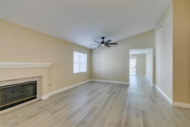 unfurnished living room featuring vaulted ceiling, a healthy amount of sunlight, light hardwood / wood-style flooring, and a tiled fireplace