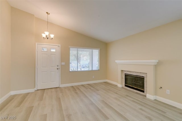 unfurnished living room featuring a tile fireplace, light hardwood / wood-style flooring, lofted ceiling, and a chandelier