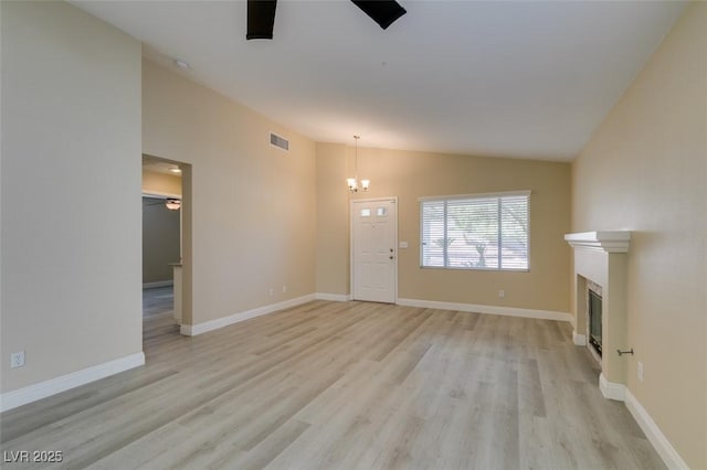 unfurnished living room with ceiling fan with notable chandelier, lofted ceiling, and light wood-type flooring