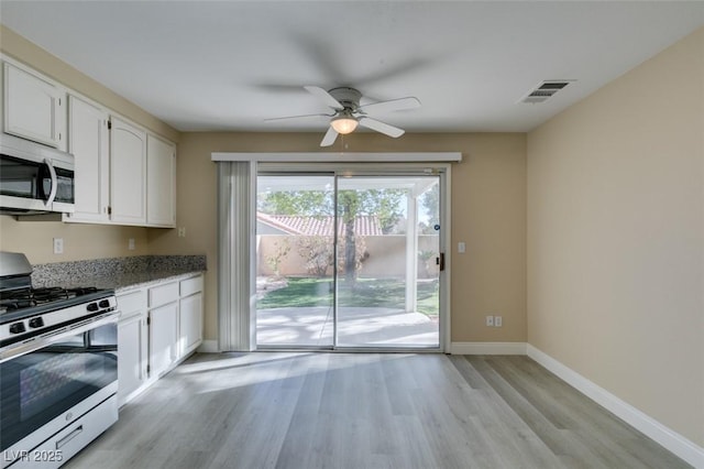 kitchen featuring stone counters, appliances with stainless steel finishes, white cabinetry, light wood-type flooring, and ceiling fan