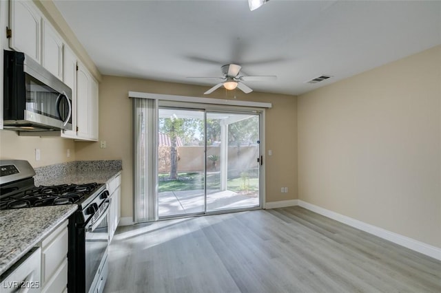 kitchen with light stone countertops, white cabinets, appliances with stainless steel finishes, light wood-type flooring, and ceiling fan