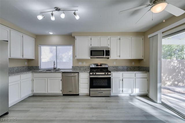 kitchen featuring appliances with stainless steel finishes, white cabinetry, a healthy amount of sunlight, sink, and light stone counters