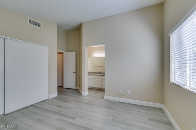 unfurnished bedroom featuring light wood-type flooring, a closet, and ensuite bath