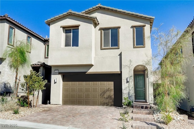 view of front of house featuring decorative driveway, an attached garage, and stucco siding