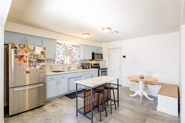 kitchen featuring decorative backsplash, a breakfast bar, appliances with stainless steel finishes, and sink