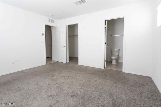 unfurnished bedroom featuring a spacious closet, light carpet, and ensuite bath