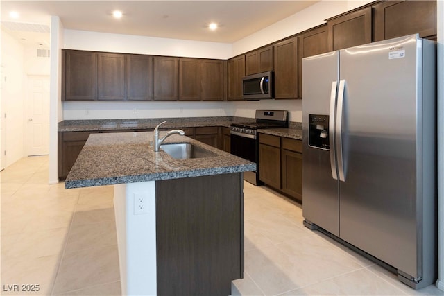 kitchen featuring appliances with stainless steel finishes, an island with sink, sink, light tile patterned floors, and dark brown cabinets