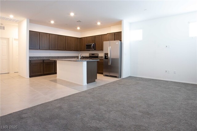 kitchen with stainless steel appliances, an island with sink, light tile patterned flooring, and dark brown cabinetry