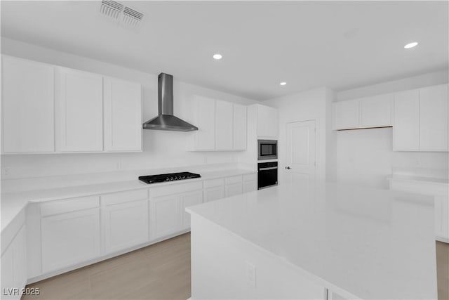 kitchen with black appliances, white cabinets, and wall chimney range hood