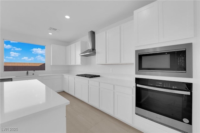 kitchen featuring built in microwave, wall chimney exhaust hood, white cabinetry, wall oven, and stainless steel gas cooktop