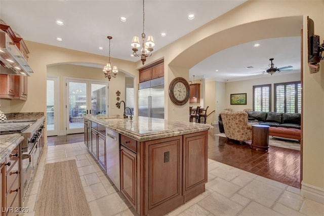 kitchen with brown cabinets, hanging light fixtures, a kitchen island with sink, stainless steel appliances, and a sink