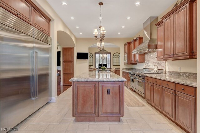 4450 Palisades Canyon Cir, Las Vegas, NV 89129 - kitchen featuring high end appliances, arched walkways, wall chimney exhaust hood, recessed lighting, and light stone countertops