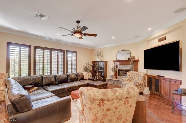 living room with ceiling fan, light hardwood / wood-style flooring, crown molding, and a premium fireplace