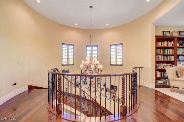 corridor featuring wood finished floors, plenty of natural light, an upstairs landing, and an inviting chandelier