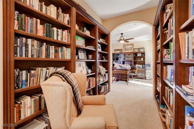 living area featuring arched walkways, light carpet, a ceiling fan, and wall of books