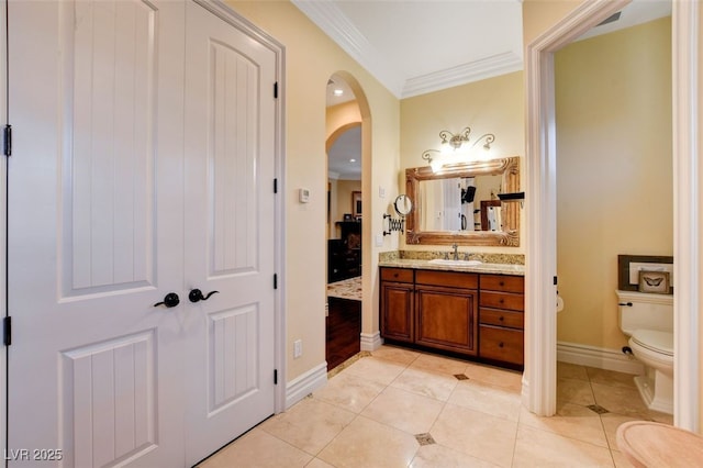 ensuite bathroom with tile patterned flooring, toilet, vanity, baseboards, and ornamental molding