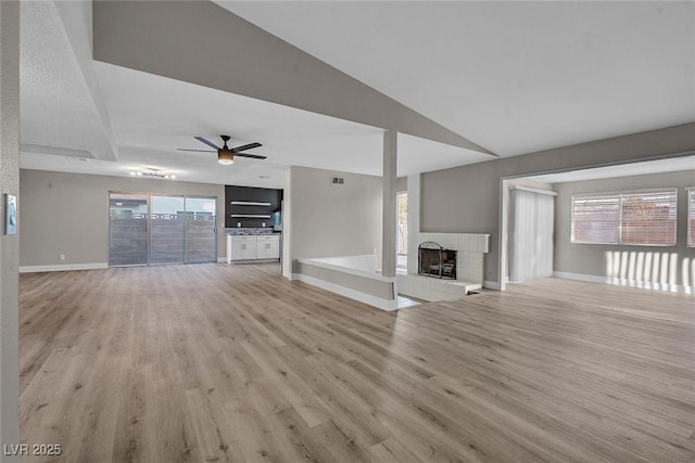 unfurnished living room with ceiling fan, a wealth of natural light, a brick fireplace, and light hardwood / wood-style floors