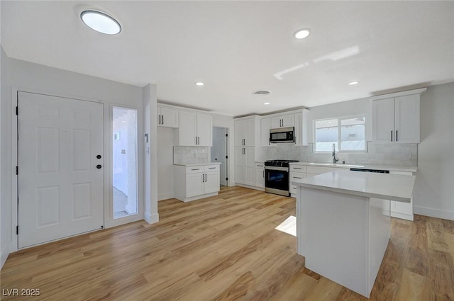 kitchen with sink, stainless steel gas range, white cabinetry, a center island, and decorative backsplash