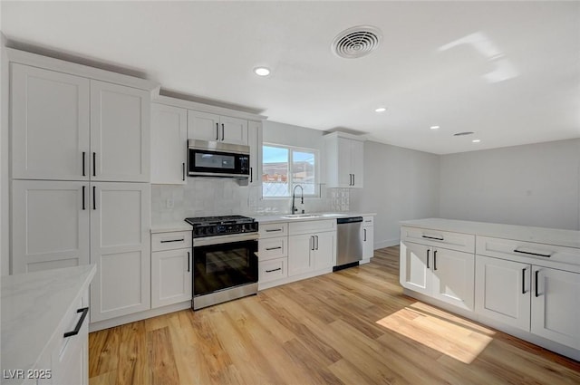 kitchen featuring sink, white cabinetry, light hardwood / wood-style flooring, stainless steel appliances, and backsplash