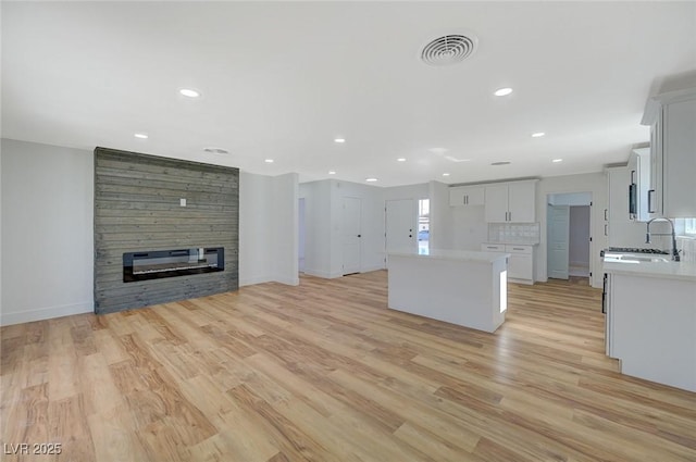 kitchen featuring a kitchen island, a fireplace, tasteful backsplash, white cabinets, and light wood-type flooring