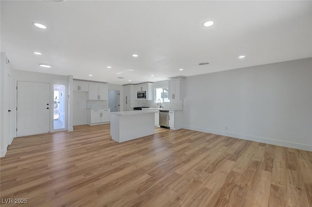 kitchen featuring tasteful backsplash, white cabinetry, a center island, stainless steel appliances, and light hardwood / wood-style flooring