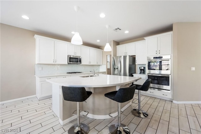 kitchen with a kitchen bar, appliances with stainless steel finishes, white cabinetry, hanging light fixtures, and a center island with sink