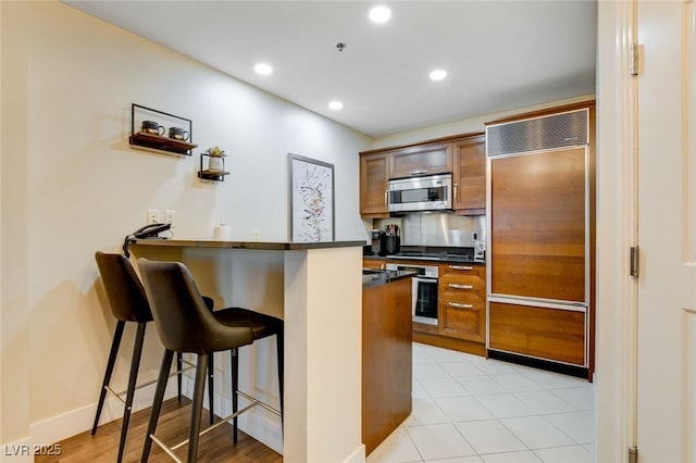 kitchen featuring light tile patterned flooring, kitchen peninsula, appliances with stainless steel finishes, and a kitchen breakfast bar