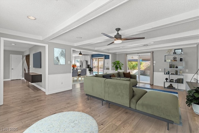 living room featuring ceiling fan, beam ceiling, wood-type flooring, and a textured ceiling