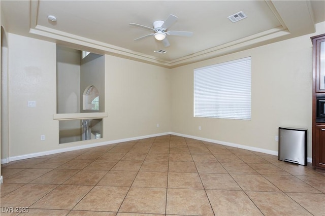 tiled empty room with ceiling fan and a tray ceiling