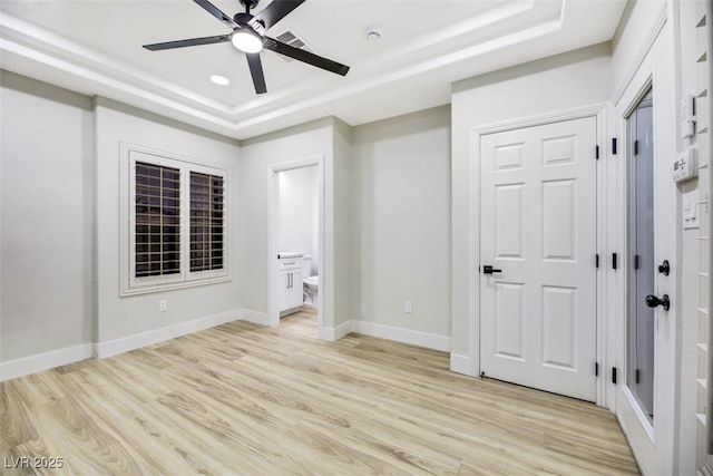 unfurnished bedroom with ceiling fan, connected bathroom, a tray ceiling, and light wood-type flooring