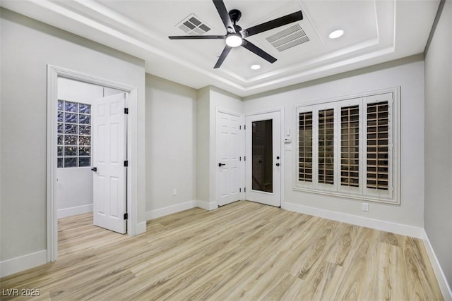 empty room with light hardwood / wood-style floors, ceiling fan, and a raised ceiling