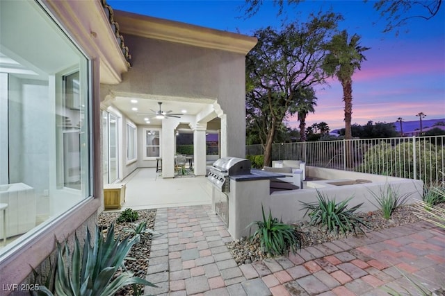 patio terrace at dusk with ceiling fan and area for grilling